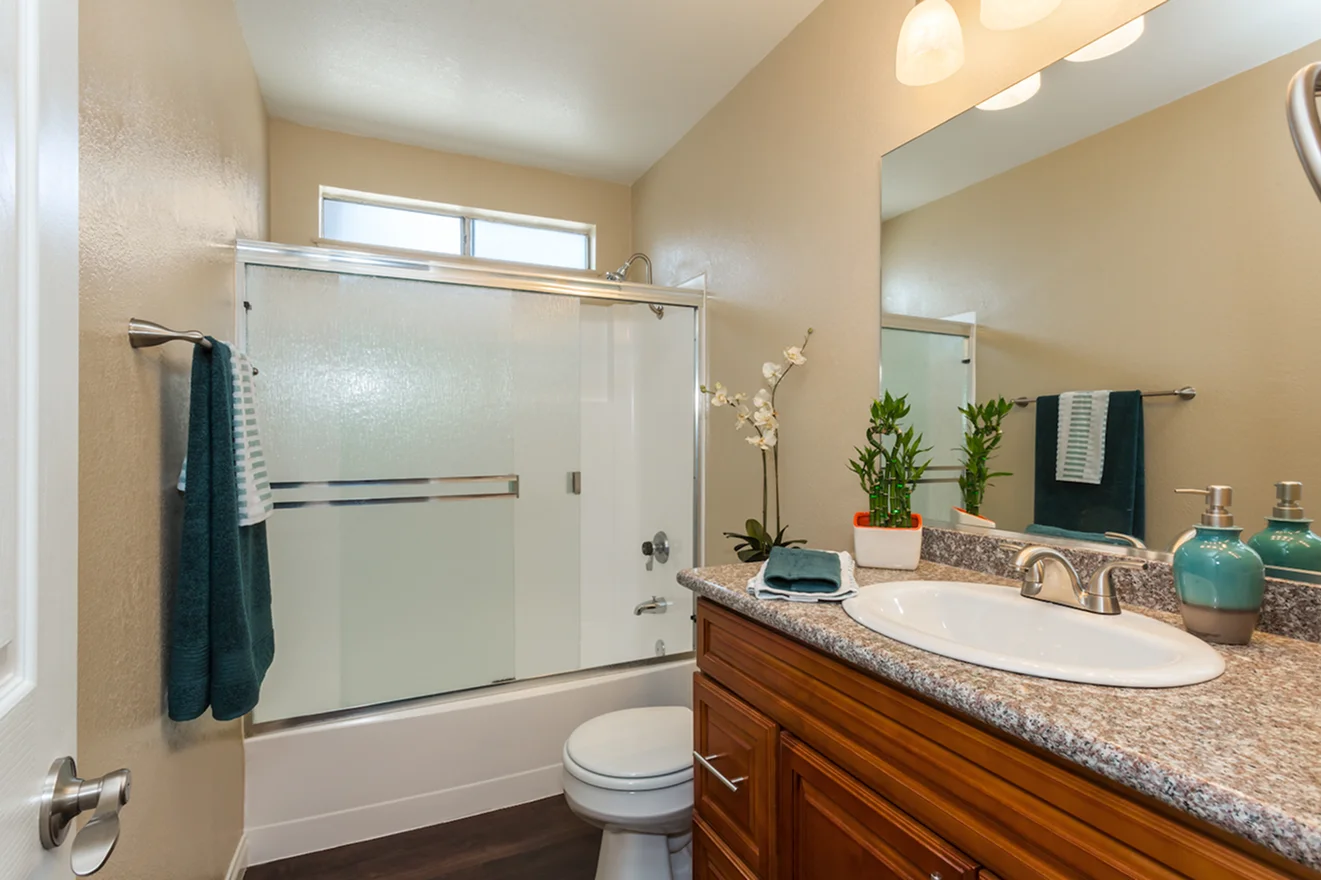Modern bathroom with granite countertop, wood vanity, and a shower-tub combo with sliding glass doors